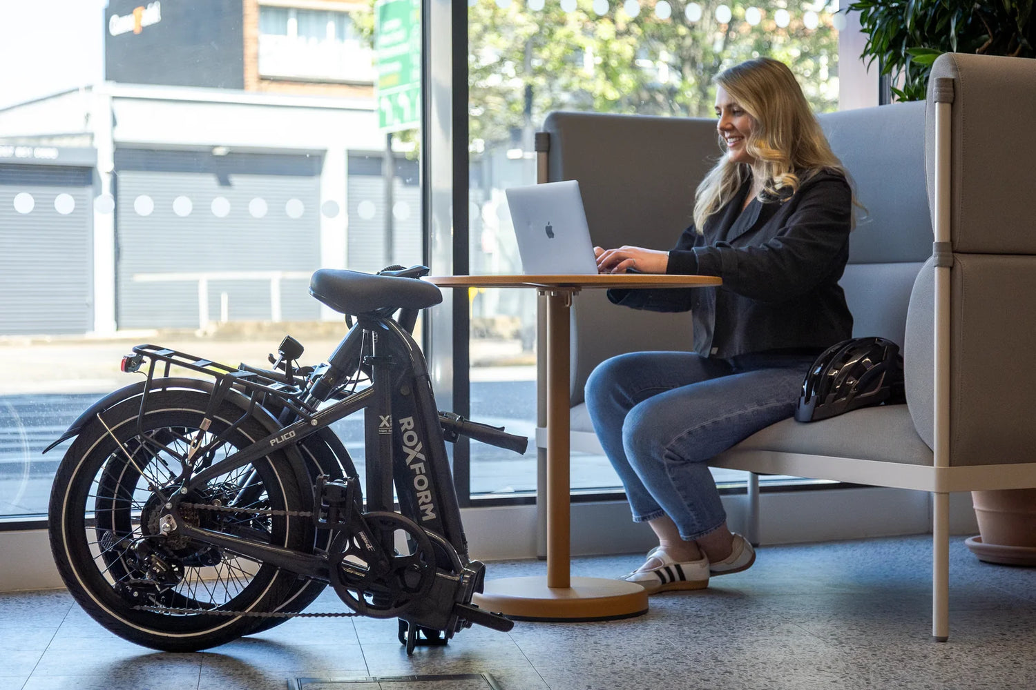 A folding Roxform e-bike stored indoors beside a desk, where the battery would be charged