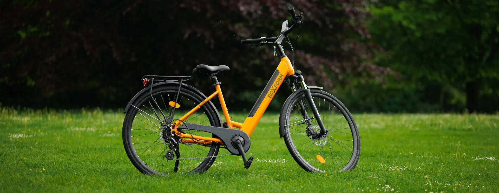 Orange electric bike on a grassy field with trees in the background
